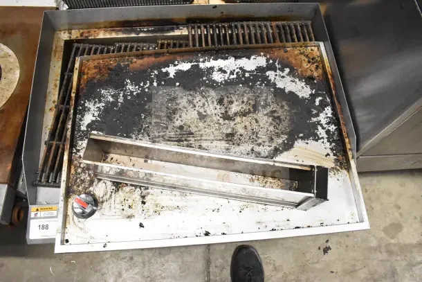 Commercial countertop gas charbroiler grill with stainless steel body, visible wear and residue, grill grates and control knob present.