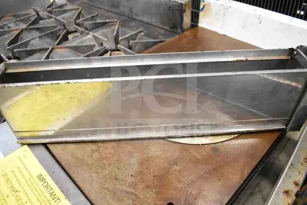 Commercial countertop gas charbroiler grill with metal grates, showing wear and rust; includes visible yellow safety label.