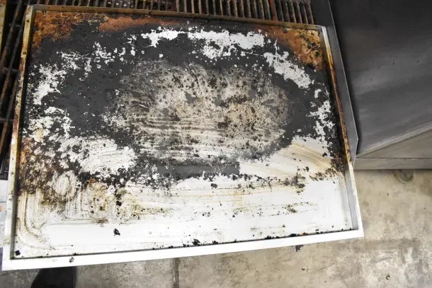 Commercial countertop gas charbroiler grill, metal surface with heavy grease buildup, showing signs of use and wear.