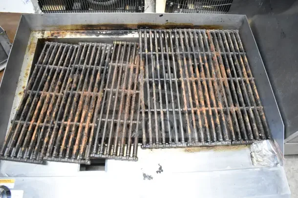 Commercial countertop gas charbroiler grill with stainless steel body and dual grates, showing signs of use.