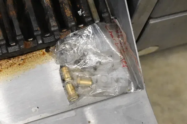 Commercial countertop gas charbroiler grill with cast iron grates, visible wear, and small brass fittings in a bag.