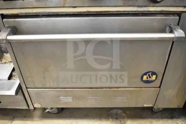US Range commercial gas-powered 6-burner range with oven, overshelf, and backsplash. Visible wear and mounted on casters.