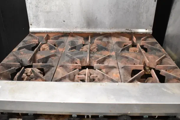 US Range commercial gas 6-burner stove with oven, overshelf, and backsplash on casters. Used condition, visible wear.