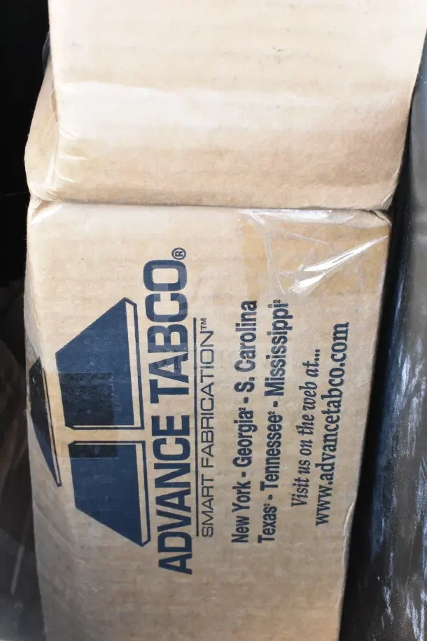 Box labeled "Advance Tabco Smart Fabrication" containing scratch and dent items, including tabletops and trash cans. Brand new condition.