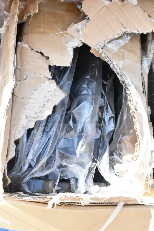 Damaged cardboard box containing brand new scratch and dent items, including tabletops and trash cans, partially visible in plastic wrap.