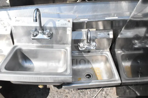 Stainless steel commercial wall mount sink with faucet, handles, and labels indicating model details; slight rust visible.