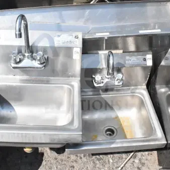 Stainless steel commercial wall mount sink with faucet, handles, and labels indicating model details; slight rust visible.