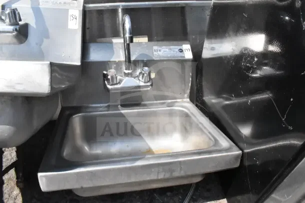 Commercial single bay wall mount sink with faucet and handles. Stainless steel, used condition, visible labels and markings.