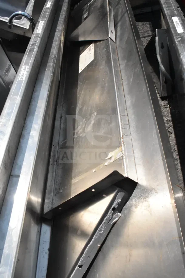 Five metal wall mount shelves in used condition with visible scratches and scuffs, featuring mounting holes and identification labels.