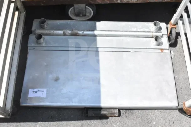 Gray metal tabletop with attached pipe fittings, showing signs of wear. Label indicates item number 257 from PCA Auctions.