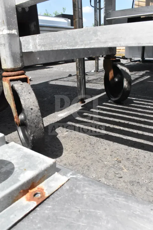 Newage Commercial Pan Transport Rack on commercial casters, showing signs of rust and wear on metal joints and wheels.
