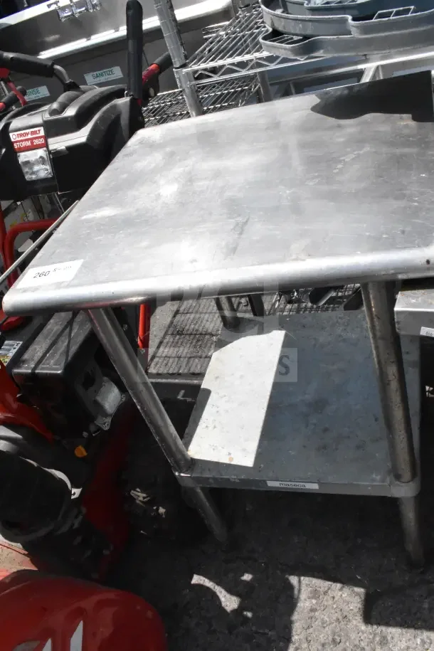 Commercial metal table with under shelf, used condition, visible wear. Features sticker "260" and "maseca" label.