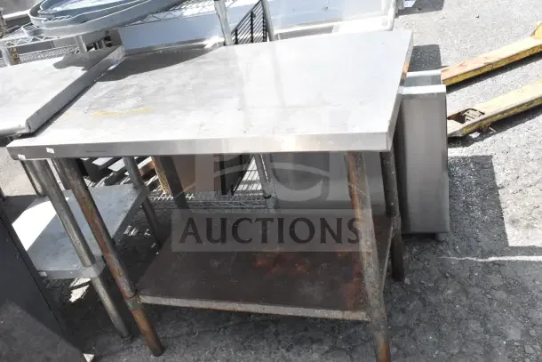 Commercial metal table with under shelf, used condition, surface wear and rust visible. Ideal for industrial use.