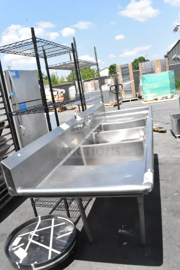 Commercial stainless steel 3 bay sink with dual drain boards, ideal for kitchen use. Good condition, outdoor setting.