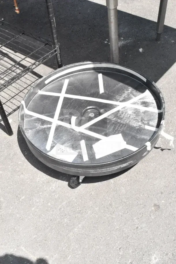 Trash Can Dolly on commercial casters, round black plastic frame, visible wear, taped markings, and a paper label.