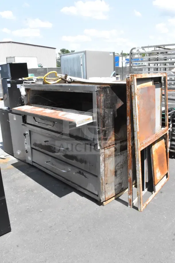 2 Bakers Pride commercial gas-powered single deck pizza ovens, weathered, outdoor setting. Handles intact, rust visible.