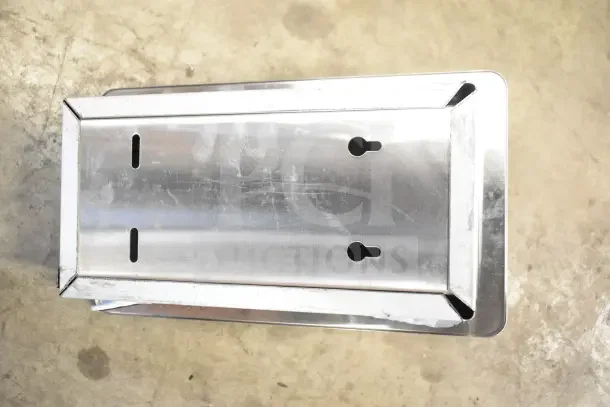 Stainless steel toilet paper dispenser, wall-mounted, keyhole slots for installation, minor surface scratches, rectangular shape.