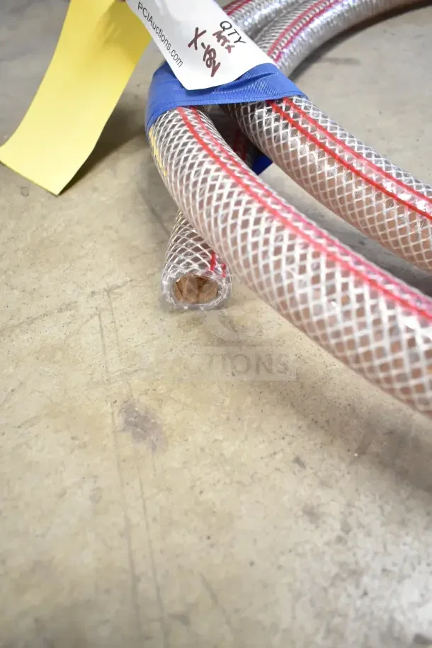 Plastic mesh hoses with red lining, new and coiled with auction lot tag indicating item number, on a concrete floor.