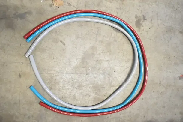 Three colored hoses laid out on a concrete floor. The hoses appear new and unused.