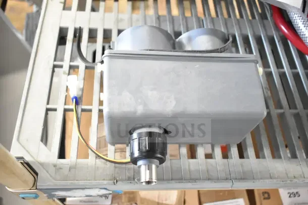 Alt text: Gray soap dispenser with dual compartments and attached wiring on a metal rack, in new condition.