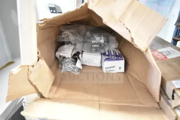 Box containing four brand new hinge sets, with visible packaging labels and hardware components, unopened.