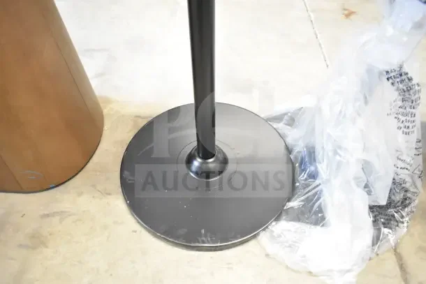 Two sturdy black metal stands on a concrete floor, one partially wrapped in clear plastic, slightly scuffed bases.
