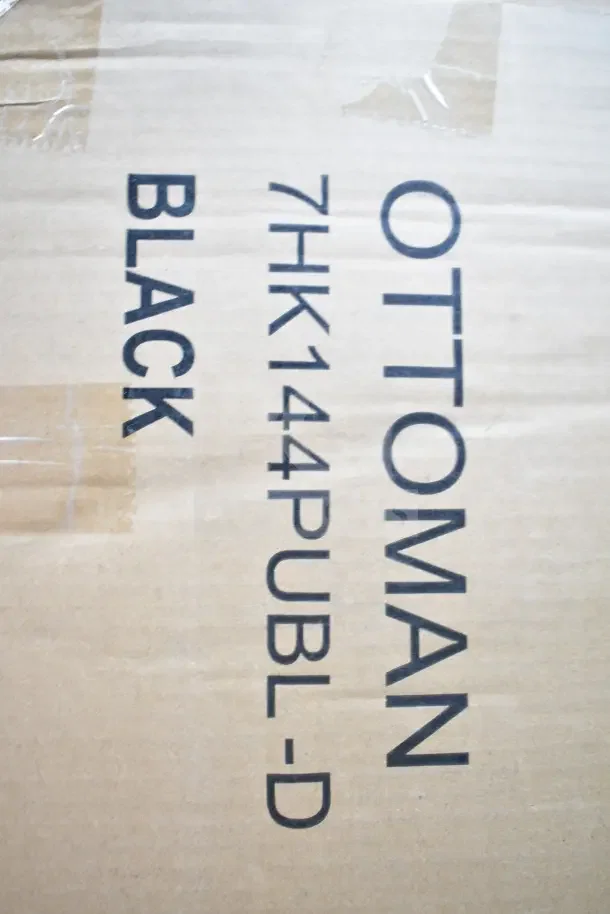 Cardboard box with "OTOMAN" and "7HK144PUBL-D BLACK" printed, indicating a brand new black ottoman with scratches and dents.