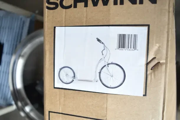 Brand new Schwinn Shuffle 26" adult scooter in white, visible through packaging with minor box damage, barcode shown.