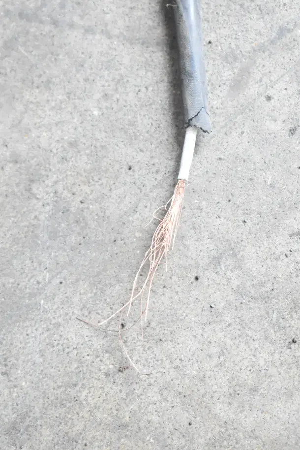 Damaged electrical cable with exposed copper wires on a concrete surface.