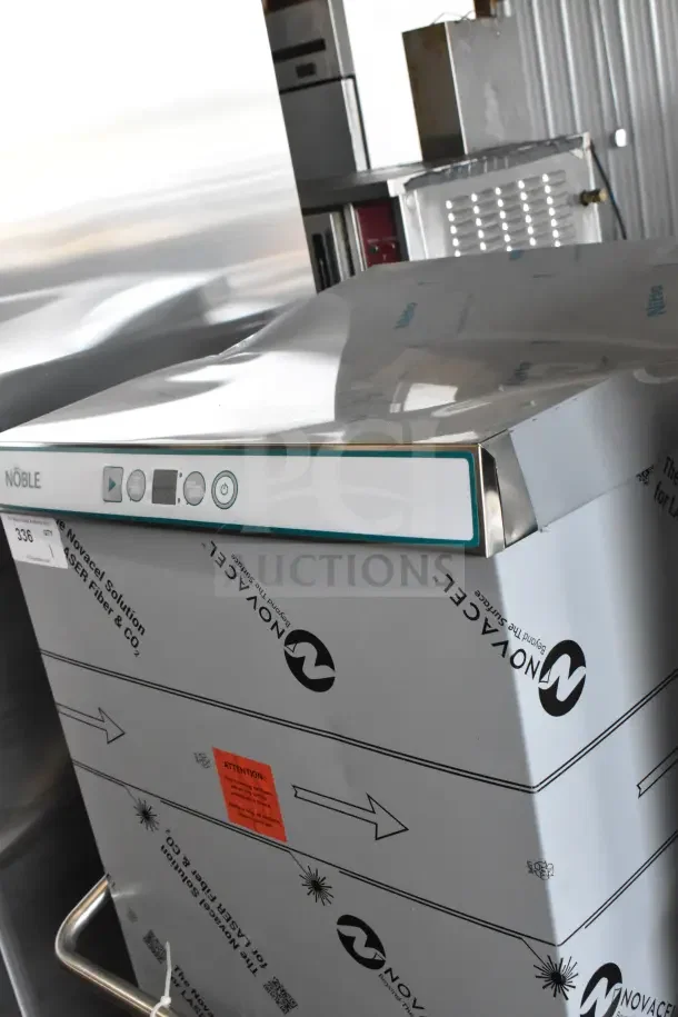 Brand new Noble commercial pass-through dishwasher with visible scratches and dents, wrapped in protective packaging.