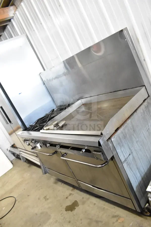 Commercial gas-powered 4 burner range with flat top griddle, 2 ovens, and backsplash. Stainless steel, good condition.
