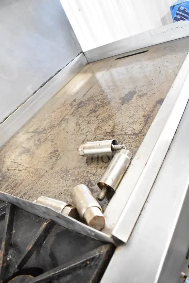 Commercial 4-burner gas range with flat top griddle, 2 ovens, and backsplash. Some visible signs of wear on surface.