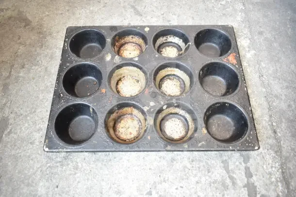 Worn muffin baking pan with 12 slots, dark finish, visible rust and wear. Part of 40 various auction items.