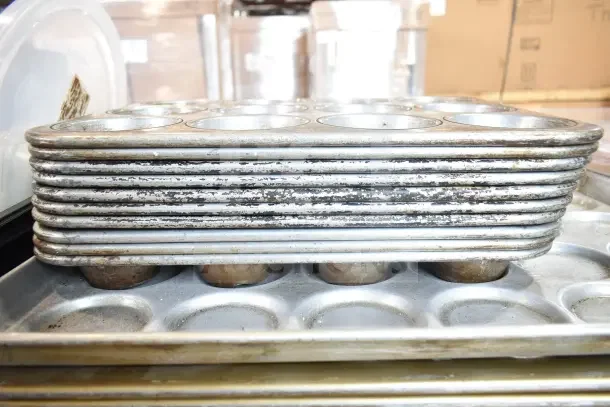Stack of used metal muffin baking pans, showing signs of wear, part of a lot of 40 various kitchen items for auction.