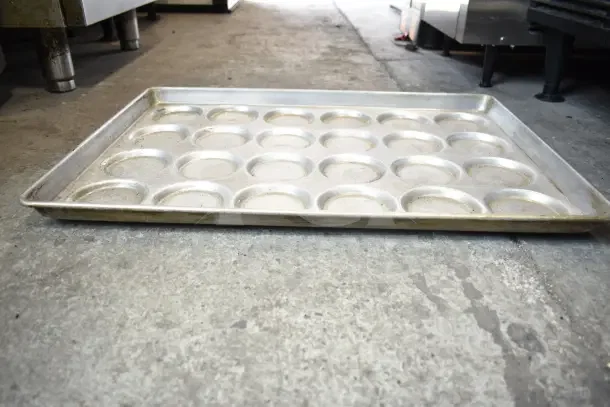 Metal muffin baking pan, 24-cup capacity, used condition on concrete floor. Part of 40-item auction lot.