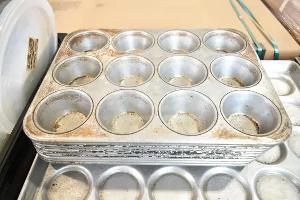 Vintage muffin baking pans, well-used with visible wear; stack of 40 items available, enhancing bid value.