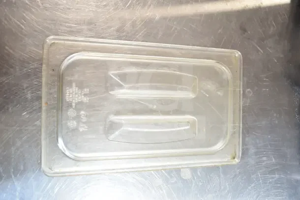 Clear plastic lid on a stainless steel surface. Part of 40 various items including muffin baking pans.