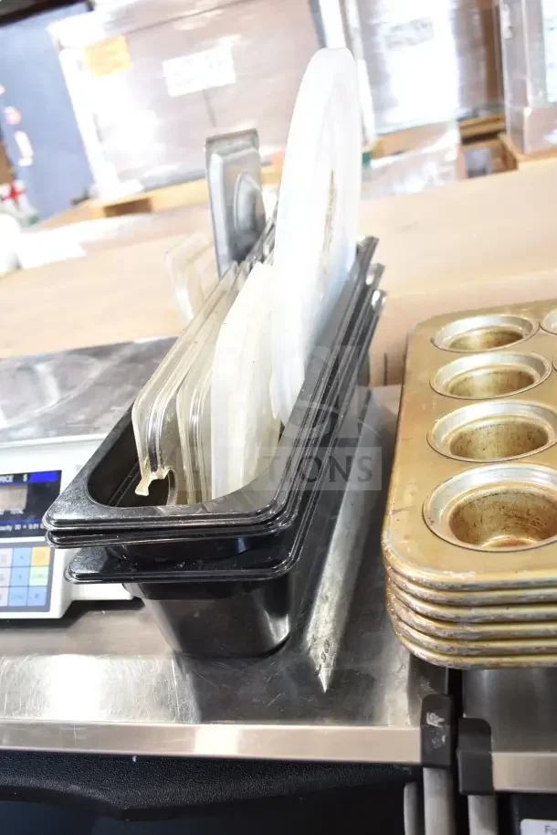 Stack of muffin baking pans and assorted kitchen items including plastic lids on a metal surface, used condition.