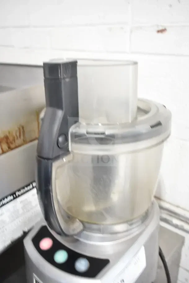 Waring countertop food processor, 120 volts, 1 phase. Features a clear plastic bowl and control panel with colored buttons. Appears in good condition.