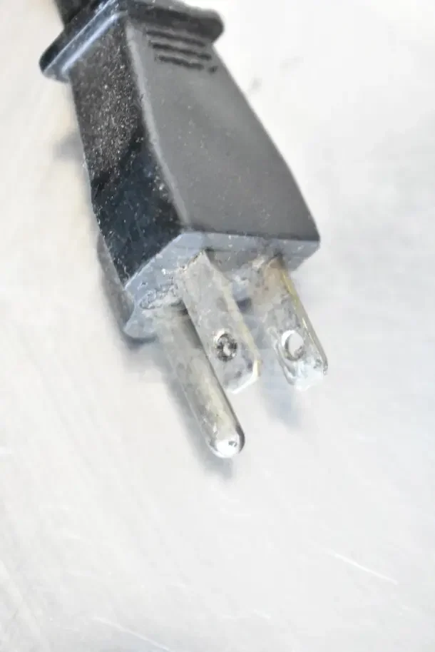 Close-up of a Waring countertop food processor power plug. Black plastic plug with three metal prongs.