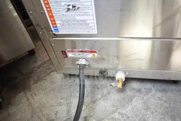 Fetco CBS-2132-XTS commercial coffee machine, metallic exterior, visible warning labels, power and water connections.