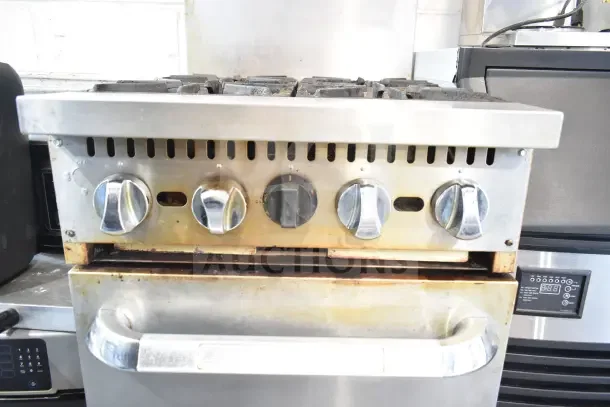 Commercial gas-powered 4 burner range with oven, over shelf, and back splash. Features stainless steel controls; moderate wear visible.