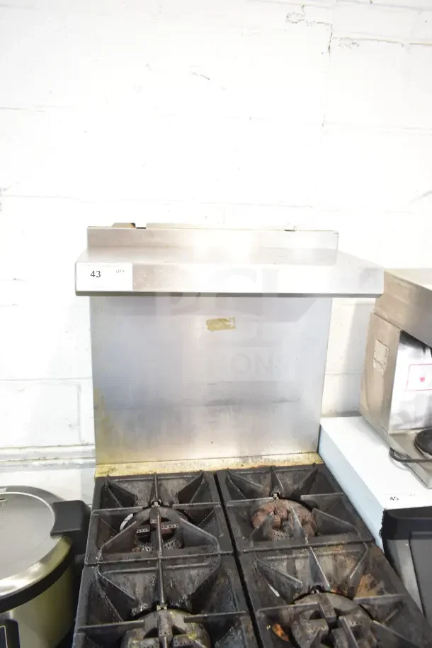 Commercial gas-powered 4 burner range with oven, over shelf, and backsplash. Used condition, metal finish. Item tag reads "43 QTY".