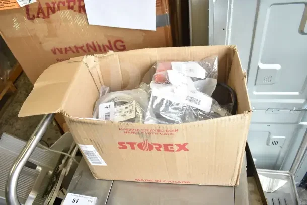 Cardboard box labeled "STOREX" containing assorted new parts like gaskets, harnesses, brackets, and knobs. Multiple item labels visible.