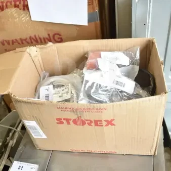 Cardboard box labeled "STOREX" containing assorted new parts like gaskets, harnesses, brackets, and knobs. Multiple item labels visible.