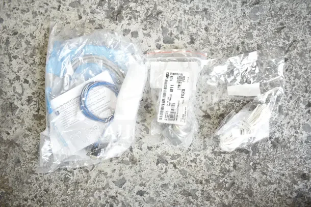 28 new scratch and dent items: gasket, millivolt harness, bracket, knob, caster. Labeled bags on concrete surface.