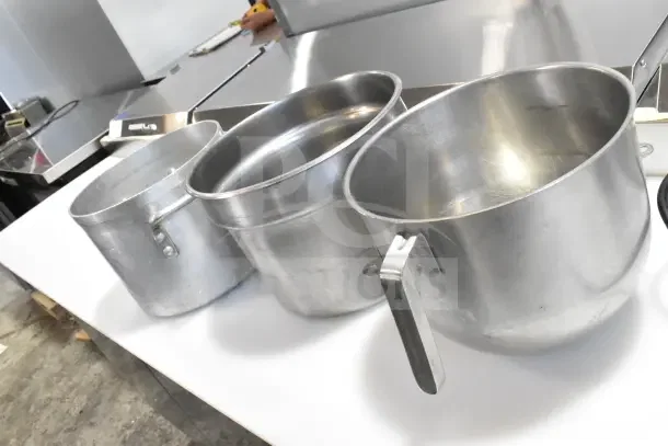 Stainless steel stock pots and mixer attachments on a table, in good condition; essential kitchen cookware set.