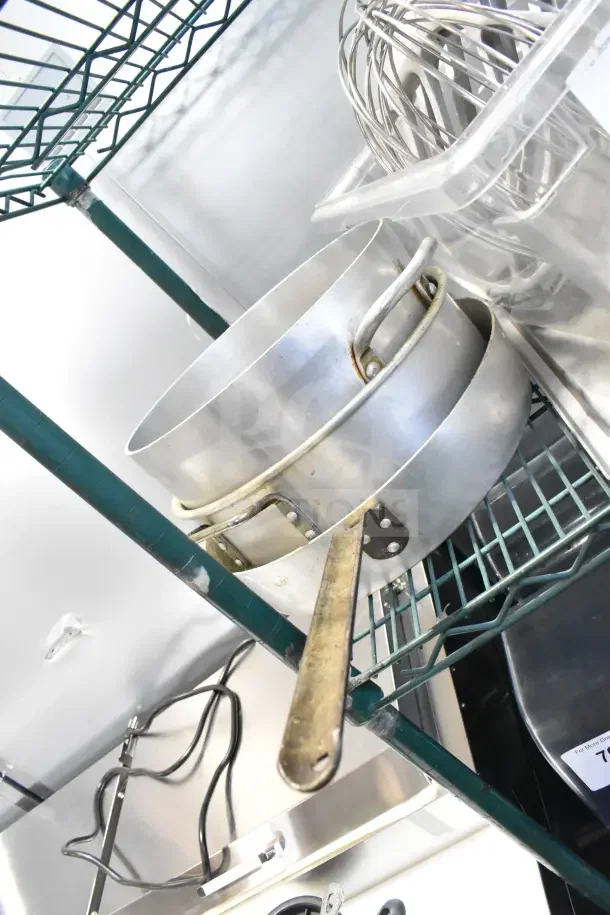 Metal stock pots and skillets on a wire shelf, alongside mixer paddle and whisk attachments, indicating kitchen use.